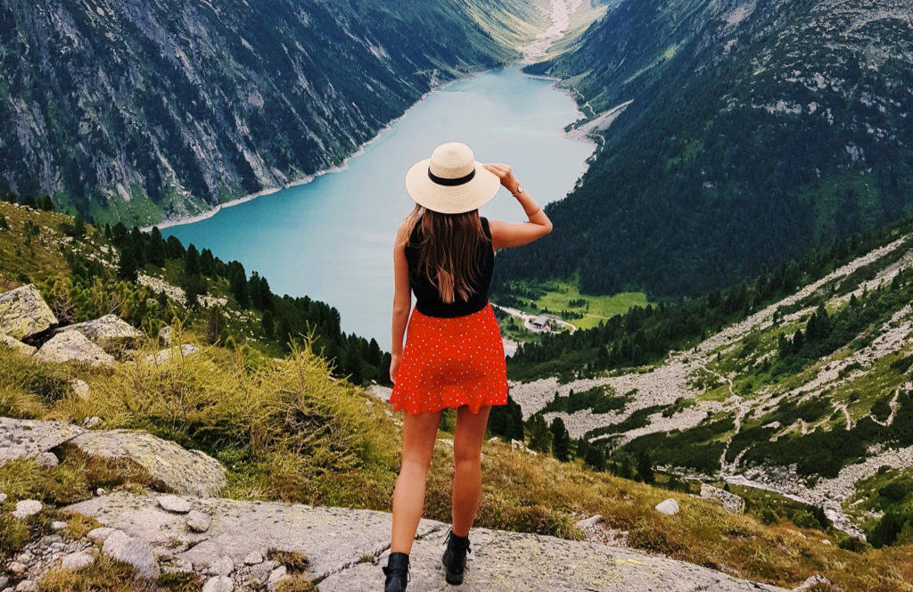 Frau steht an einer Bergspitze und bewundert die Aussicht auf einen Bergsee