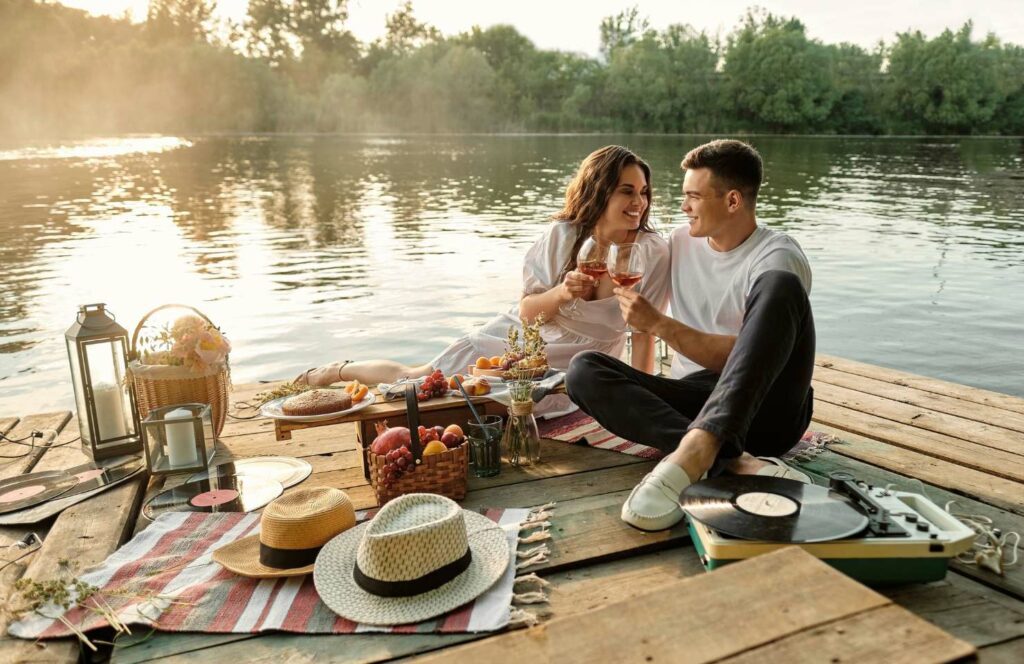 Pärchen sitzt auf einem Steg und hat ein romantisches Picknick bei Sonnenuntergang