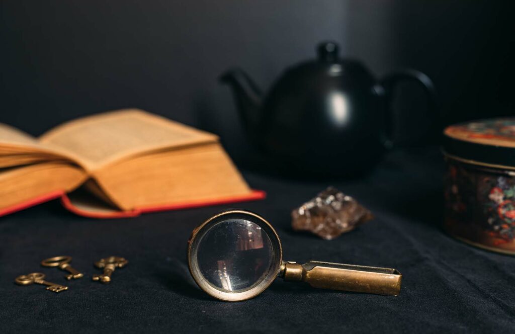 Collection of mysterious objects on a black background: book, keys, magnifying glass, crystal, box and teapot.