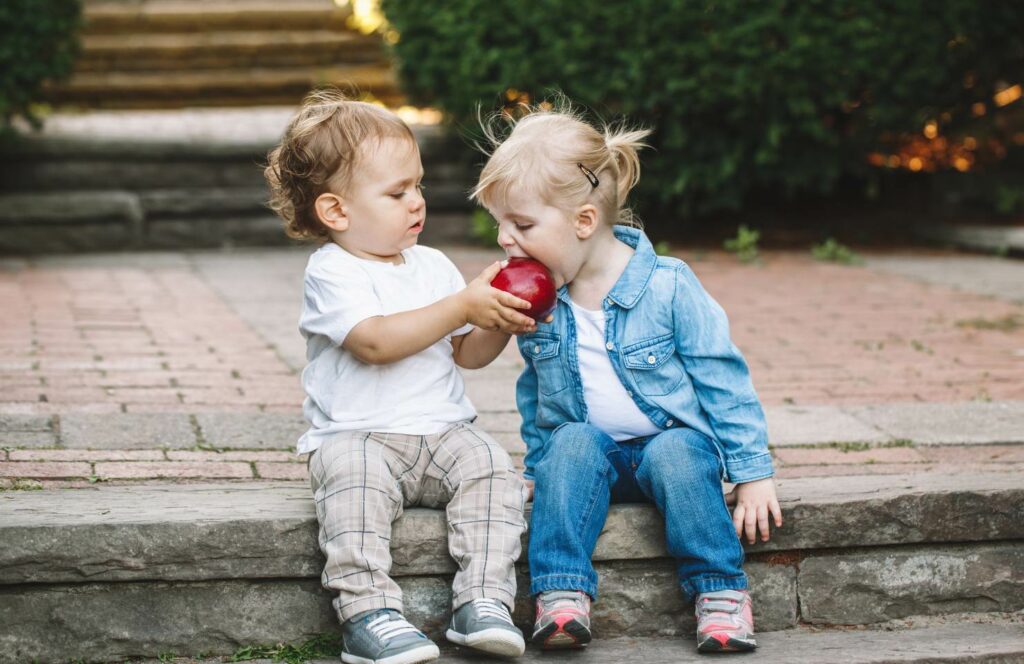 Kleinkinder die befreundet sind und sich einen roten Apfel teilen