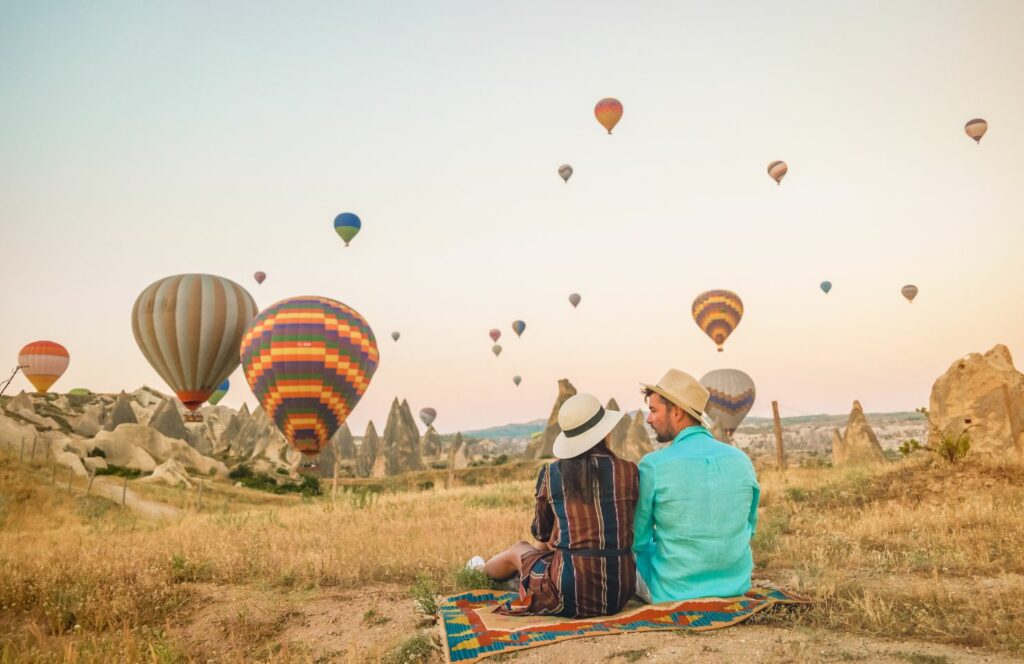 Paar sitzt auf einem Feld voller Heißluftballons