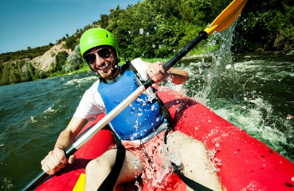 Mann mit grünem Helm und blauer Schwimmweste im Kanu 