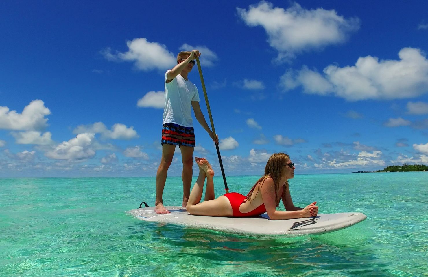 man is standing on sup board and woman is lying escape the routine
