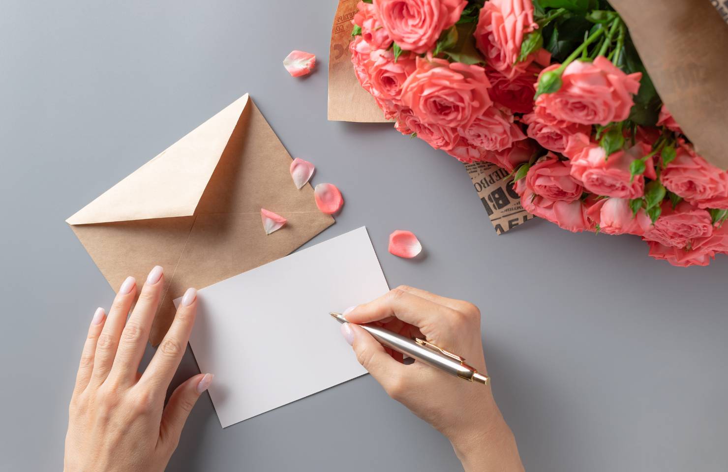 Woman beginning to write in a gift card with a bouquet of flowers