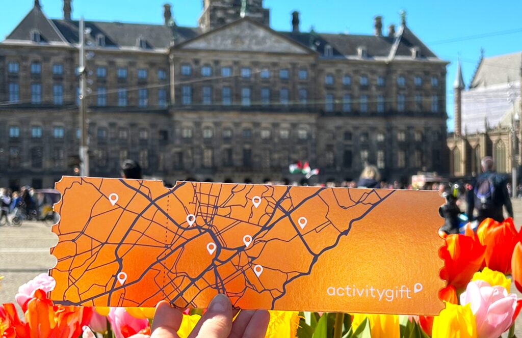 Tarjeta del cheque-regalo-actividad delante de los tulipanes de la plaza Dam de Ámsterdam