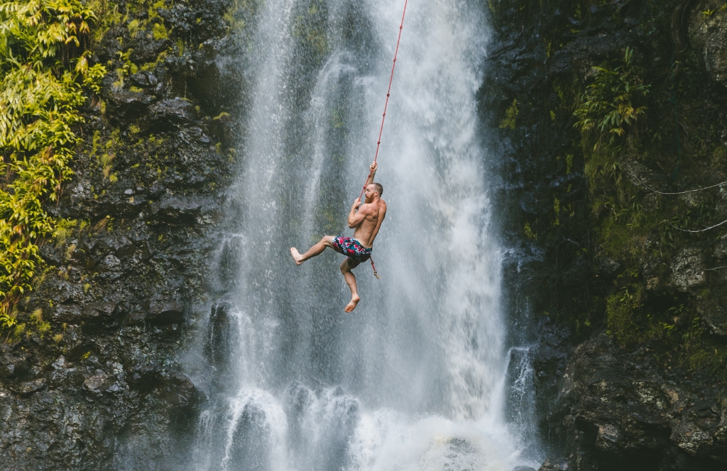 A man swings on a vine in front of a waterfall with one of the best activity gift cards for siblings: an Experience Gift.