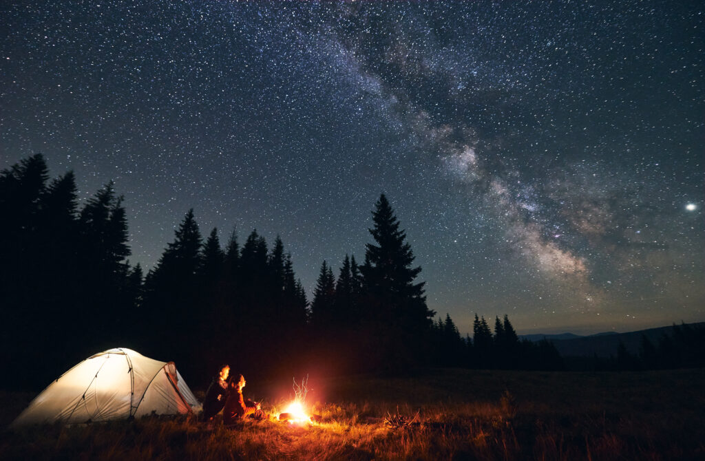 Couple assis devant un feu de camp et à la belle étoile en train de camper